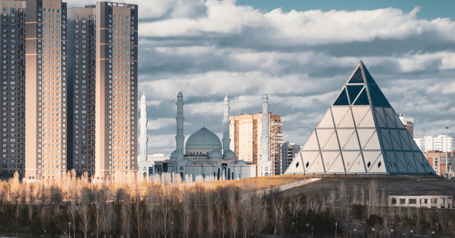The glass pyramid of Astana's Palace of Peace beside a white mosque and towers