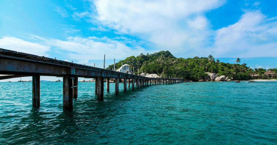 A long jetty stretching over turquoise water toward a green tropical island