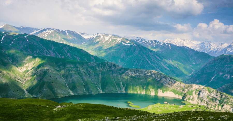 A deep-green mountain lake among lush peaks and snow-capped ridges in Kazakhstan