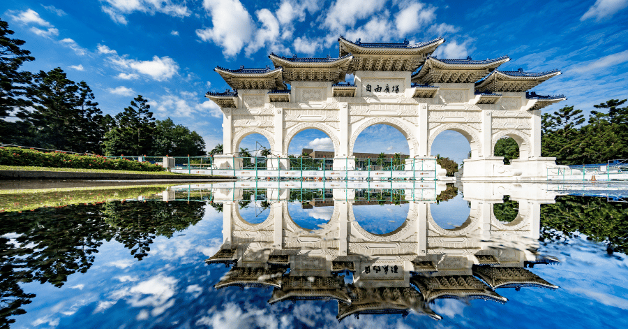 The white Liberty Square archway with blue-tiled roofs reflected in still water at Chiang Kai-shek Memorial Hall, Taipei