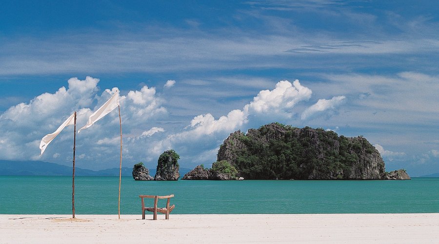 A chair and white flags on the empty white sand of Tanjung Rhu, with a limestone islet offshore