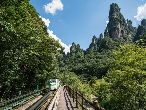 A green sightseeing monorail running through the Ten Mile Gallery valley below sandstone peaks