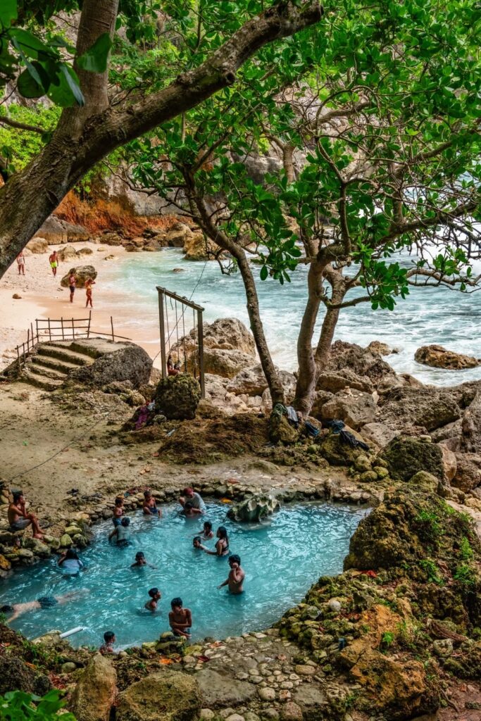Visitors bathing in the natural freshwater pool at Tembeling, with the beach beyond the trees