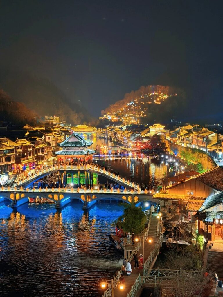 Fenghuang Ancient Town's riverside stilt houses and arched bridge lit up at night