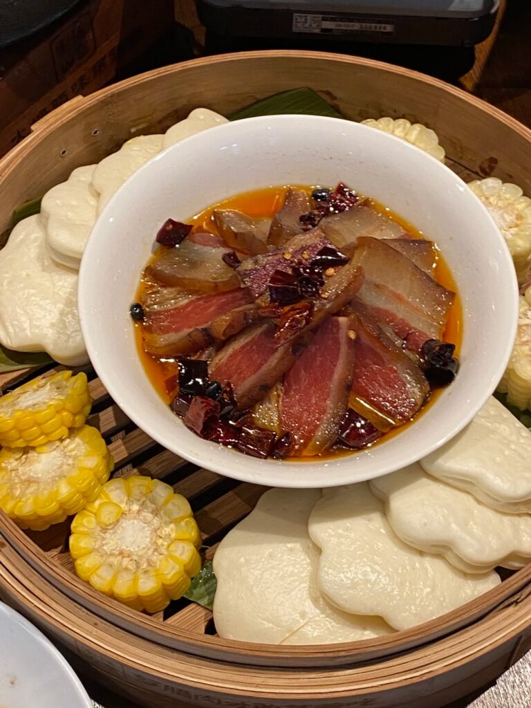 Sliced Tujia smoked cured pork in chilli oil, served with steamed buns and corn