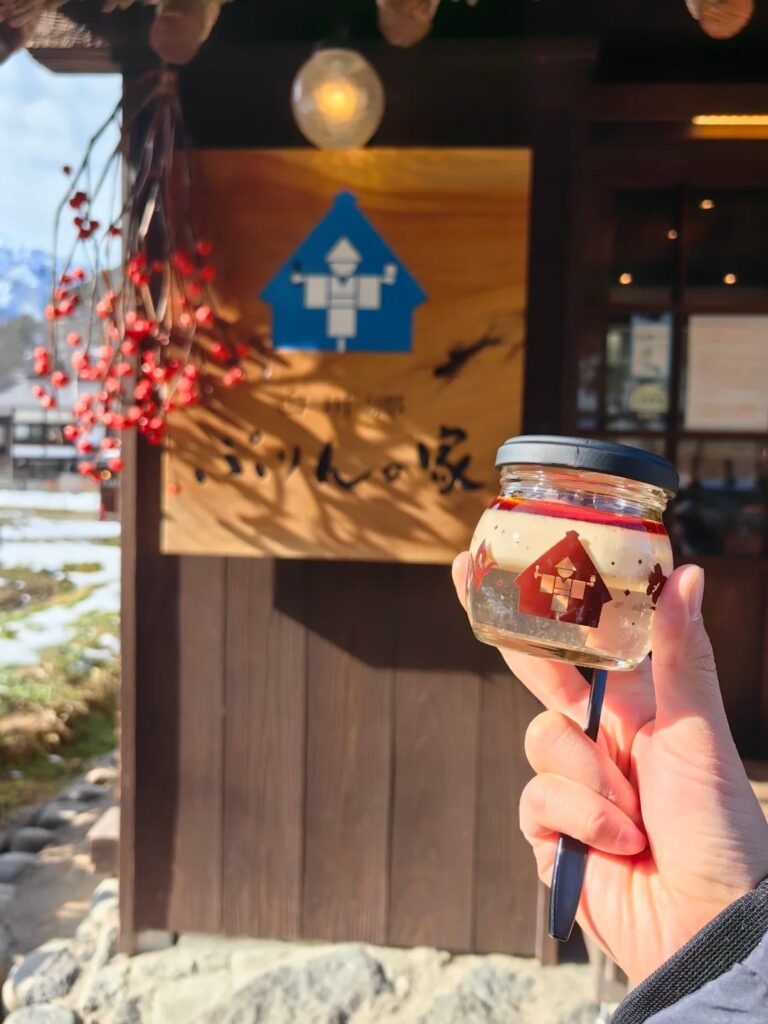 A jar of Mizu Purin pudding held up outside the Shirakawago Purin no Ie shop