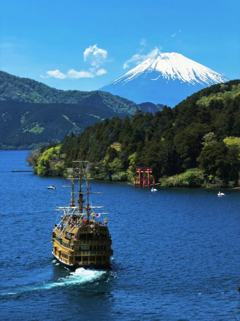 A golden pirate sightseeing ship on Lake Ashi with Mt Fuji and the red lake torii behind