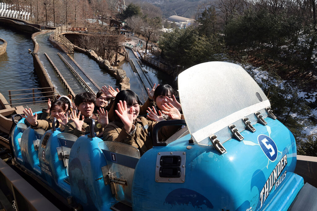 Riders raise their hands in a blue Thunder Falls flume boat above a snowy channel