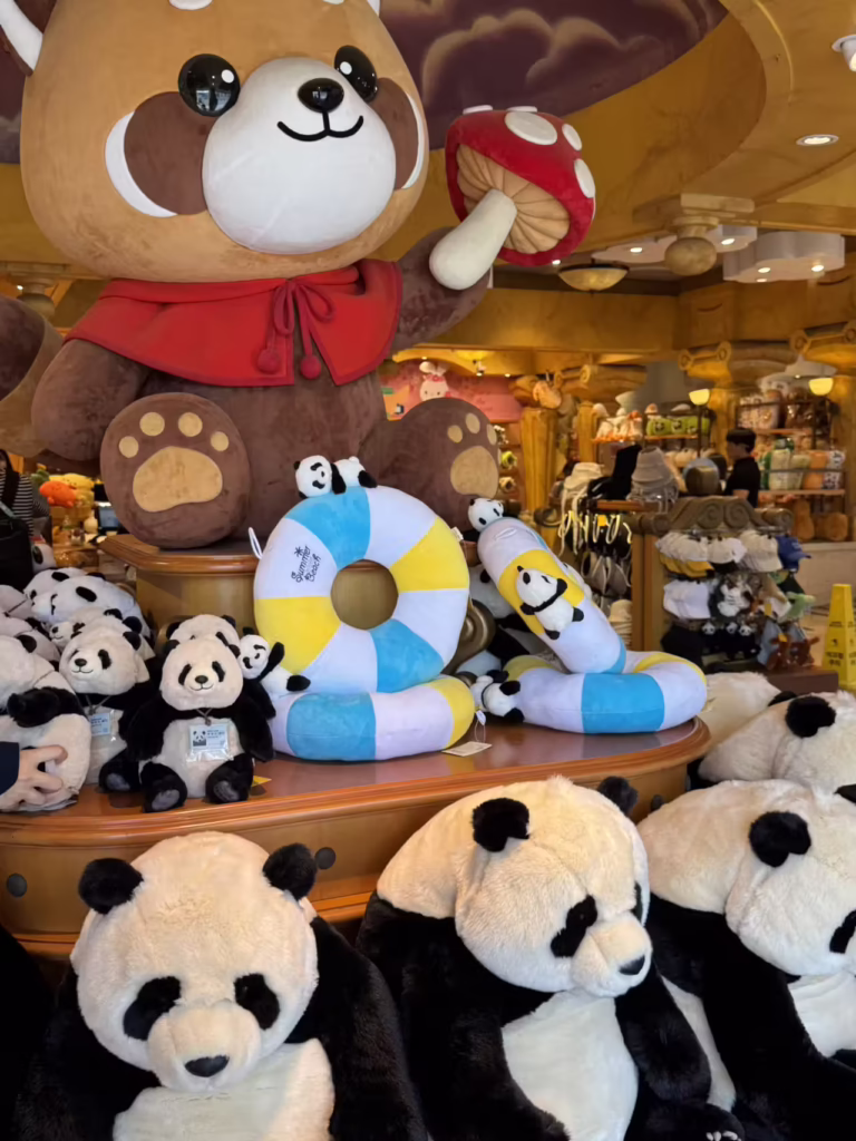 Panda soft toys stacked below a large bear mascot statue holding a mushroom