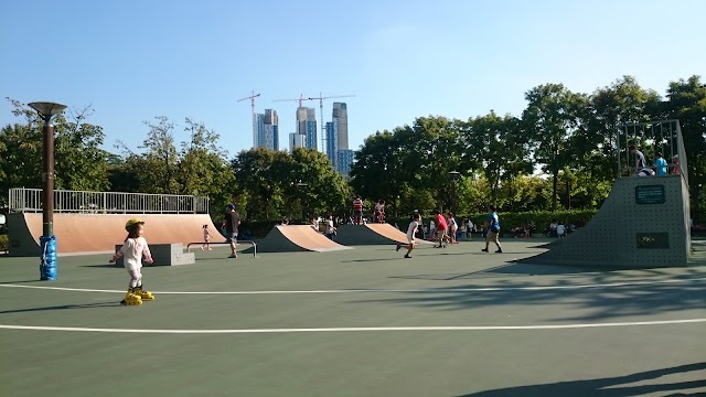 Skaters on ramps at an outdoor concrete skate park with tower blocks behind