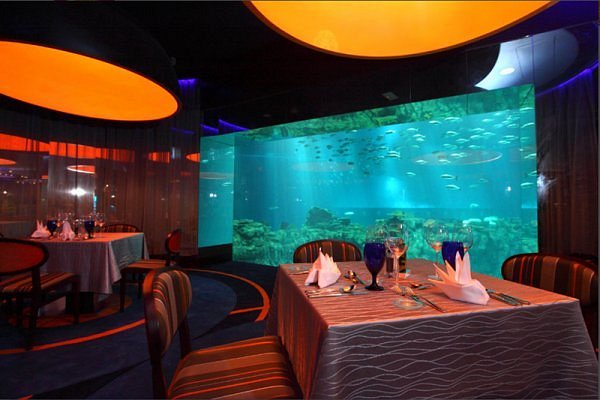 Dining tables set with wine glasses in front of the glowing Grand Aquarium tank at Neptune's