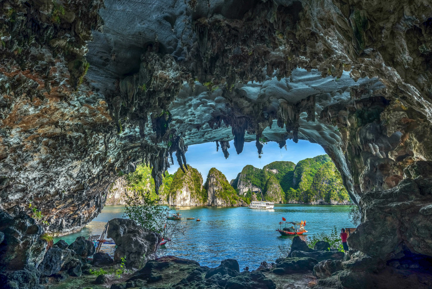 View out through a stalactite-fringed cave mouth to karst islands and small boats