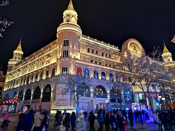 A grand illuminated European-style building on Harbin's Central Street at night, crowds below
