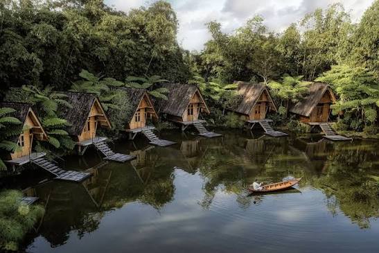 Row of stilted bamboo huts along a still lake with a small wooden boat