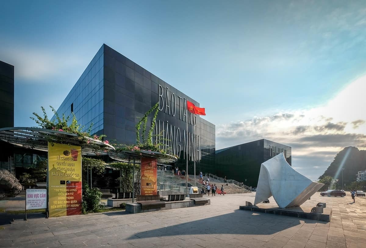 The black glass facade of Quang Ninh Museum with its plaza, banners and a Vietnamese flag