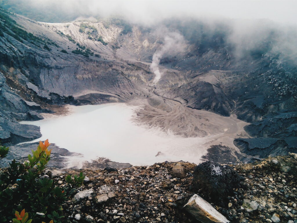 Steam venting beside a pale mineral lake on the ash-grey floor of Tangkuban Perahu's crater