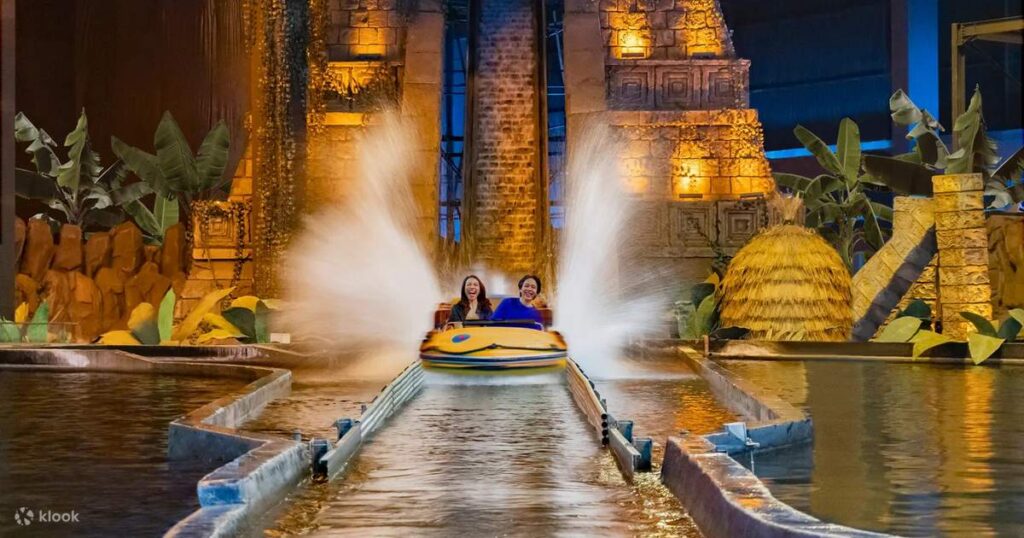 Two riders sending up spray on an indoor water ride between stone temple sets