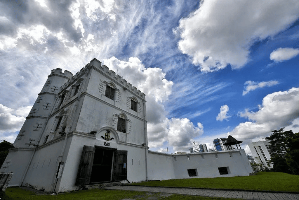 Whitewashed Fort Margherita with crenellated tower and arched doorway under a cloudy sky