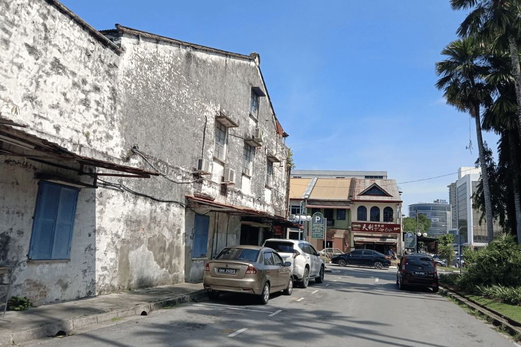 Weathered whitewashed shophouse with blue shutters on a quiet Jalan Padungan street