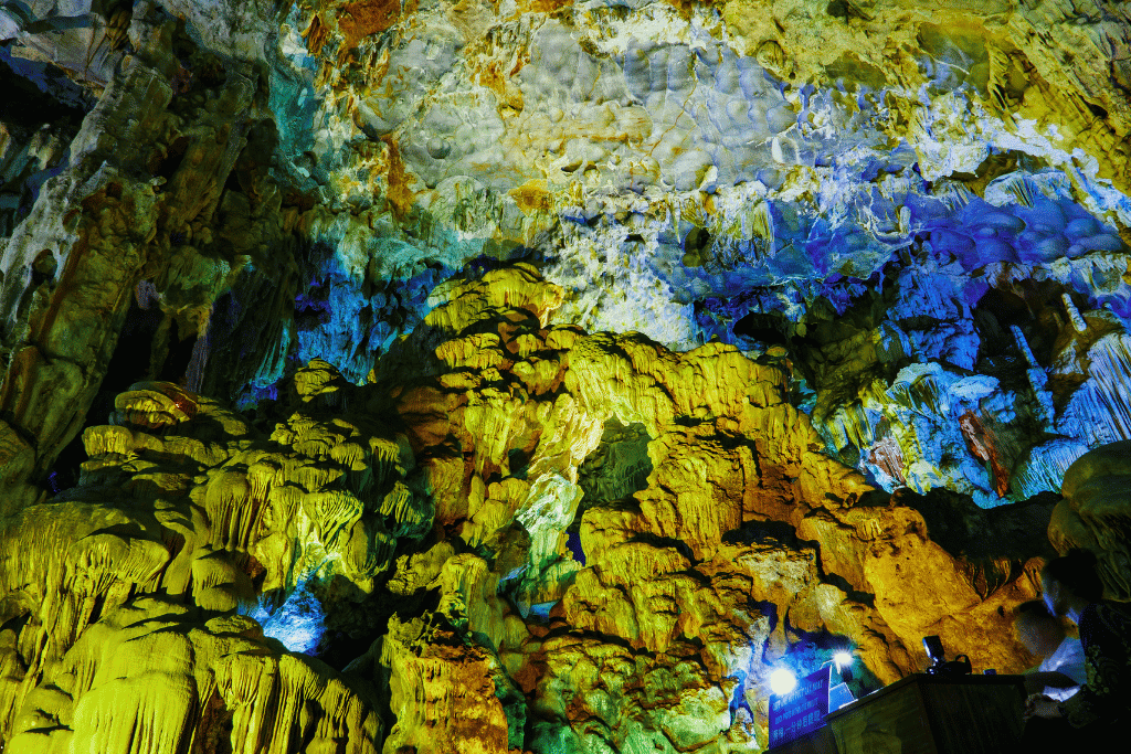 Stalactites and cave walls lit in yellow, blue and green inside Sung Sot Cave