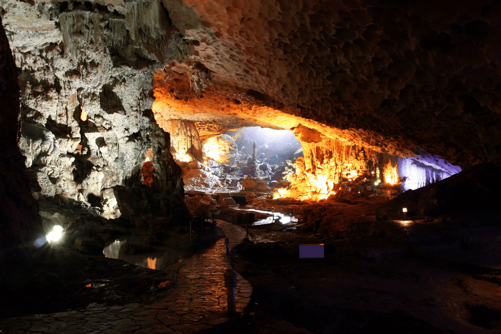 Paved walkway through a large cave chamber lit in warm orange, Thien Cung Cave