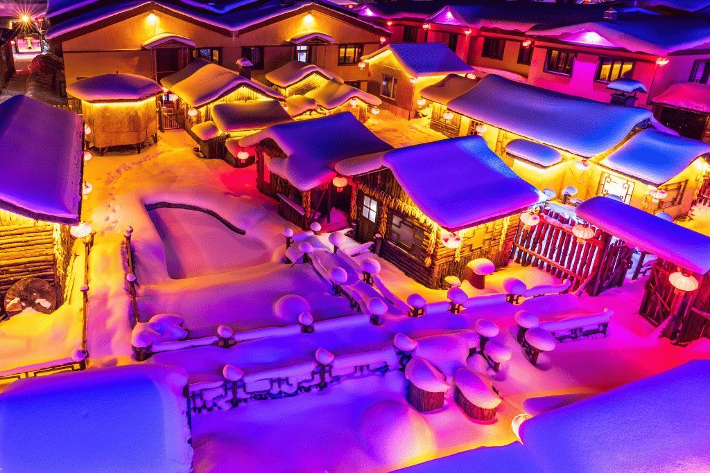 Snow-laden village rooftops lit purple and orange at night in China Snow Town
