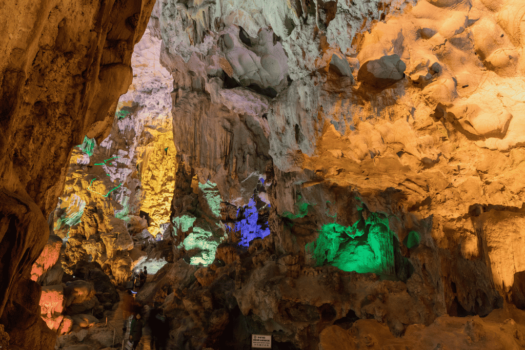 Cave formations lit in green, blue and amber inside Dau Go Cave