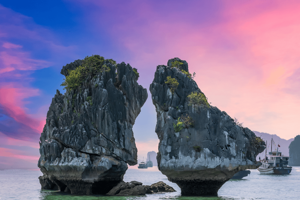 Two limestone stacks leaning towards each other at sunset, a cruise boat passing behind