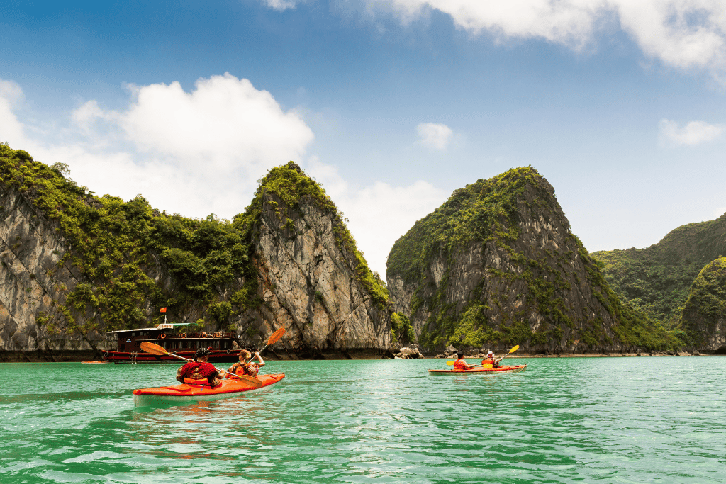 Two orange kayaks on green water between forested limestone cliffs