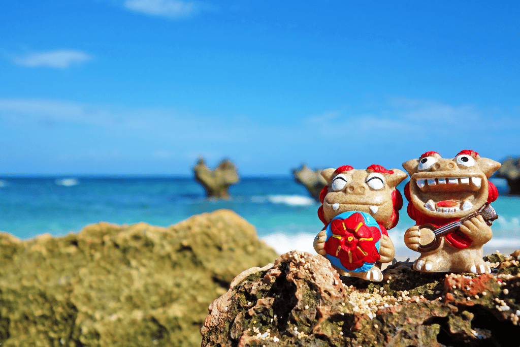 Two ceramic shisa lion-dog figurines on coral rock above a turquoise Okinawan sea