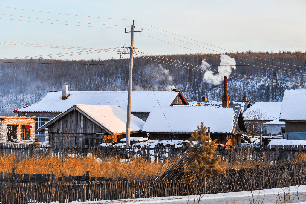 Snow-covered wooden houses with smoking chimneys and forested hills in China's far north