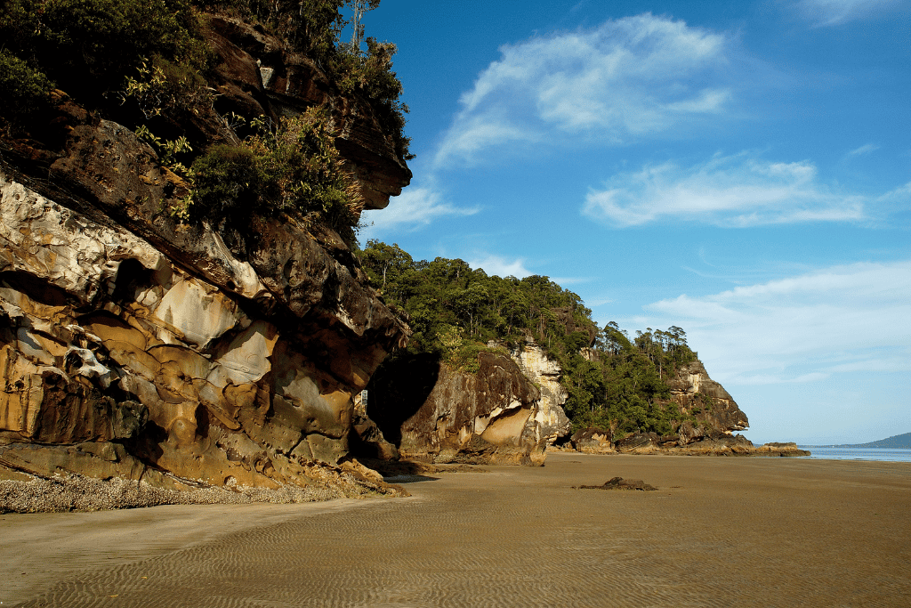 Layered sandstone cliffs and jungle meeting an empty beach at low tide in Bako National Park