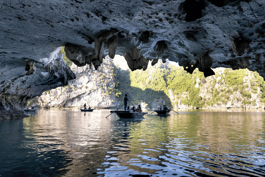Rowing boats passing beneath a wide stalactite-hung cave overhang into sunlit water