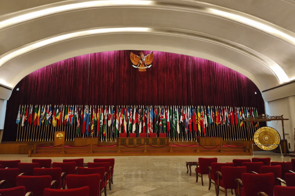 Conference hall lined with rows of national flags, red curtain and red seating