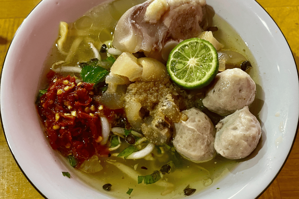 Bowl of clear beef noodle soup with meatballs, tendon, bean sprouts, chilli and lime