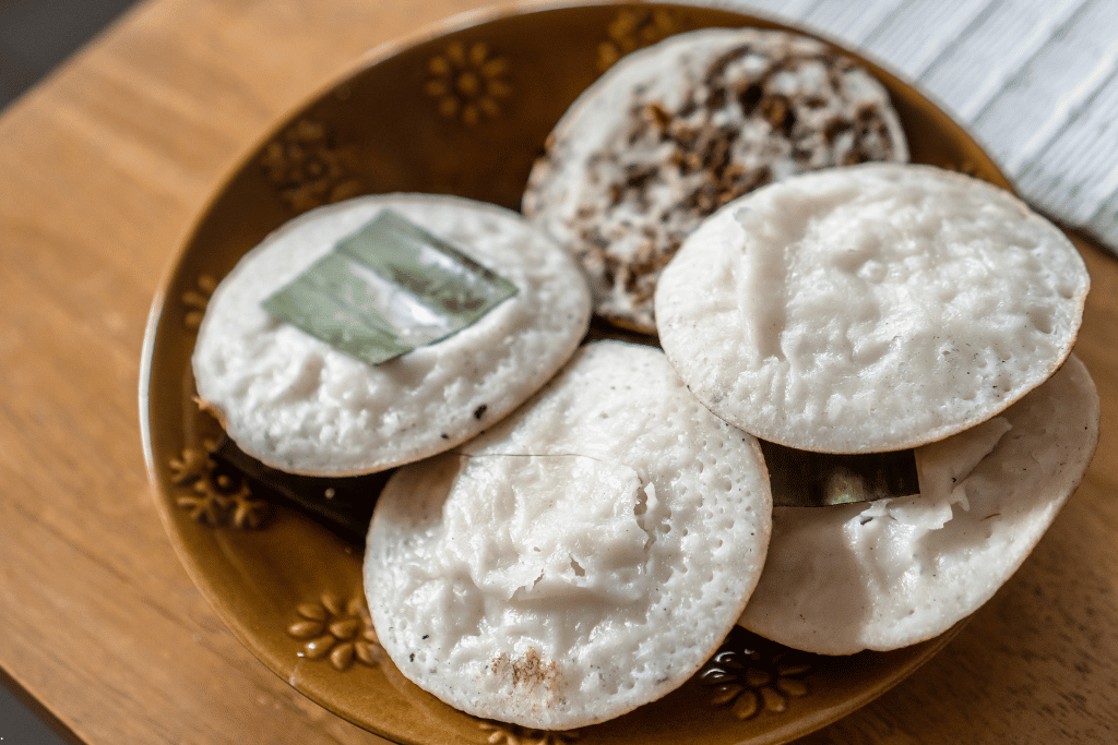 Round white surabi pancakes on a brown plate, one topped with dark oncom