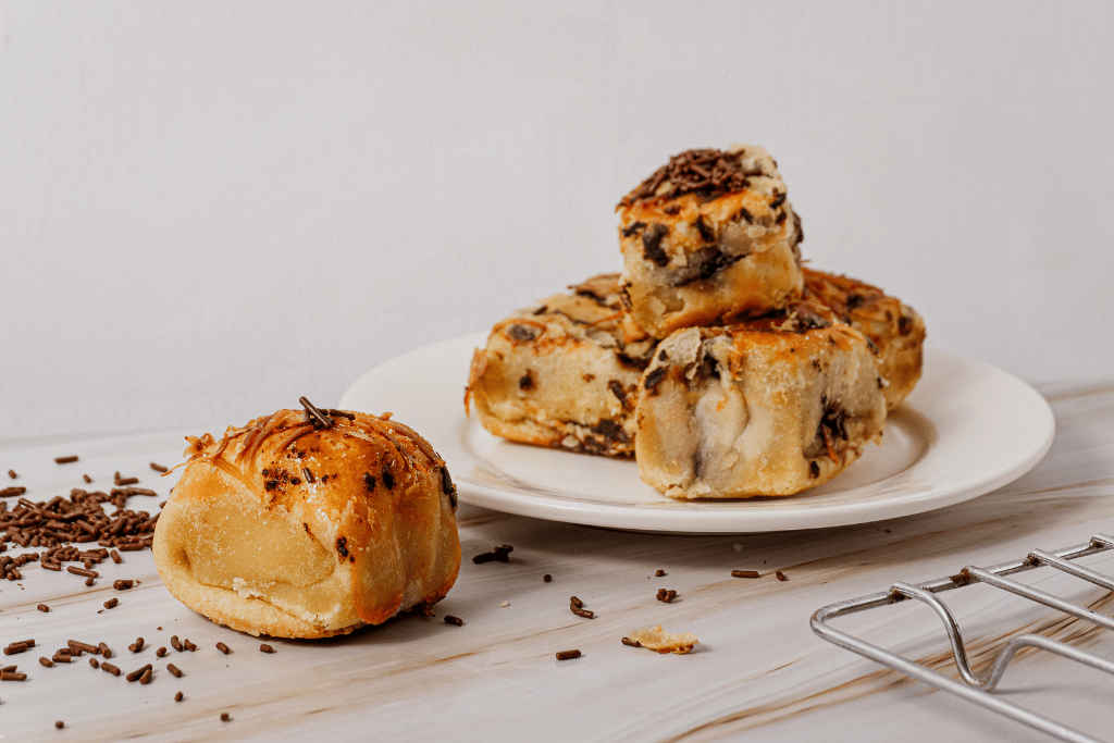 Flaky pisang bolen pastries topped with chocolate sprinkles on a white plate