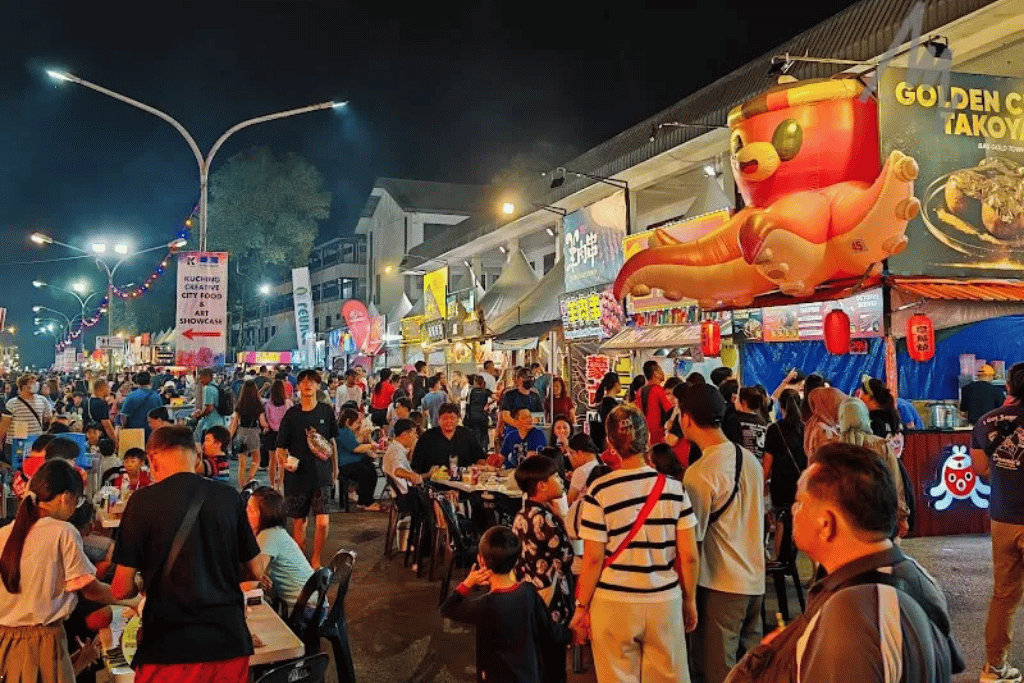 Crowded night food fair with lit stalls, diners at tables and a giant inflatable octopus sign