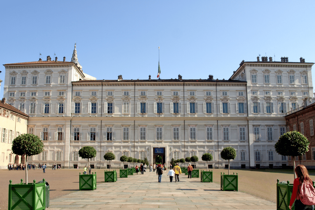 A grand white royal palace facade fronted by a topiary-lined gravel forecourt