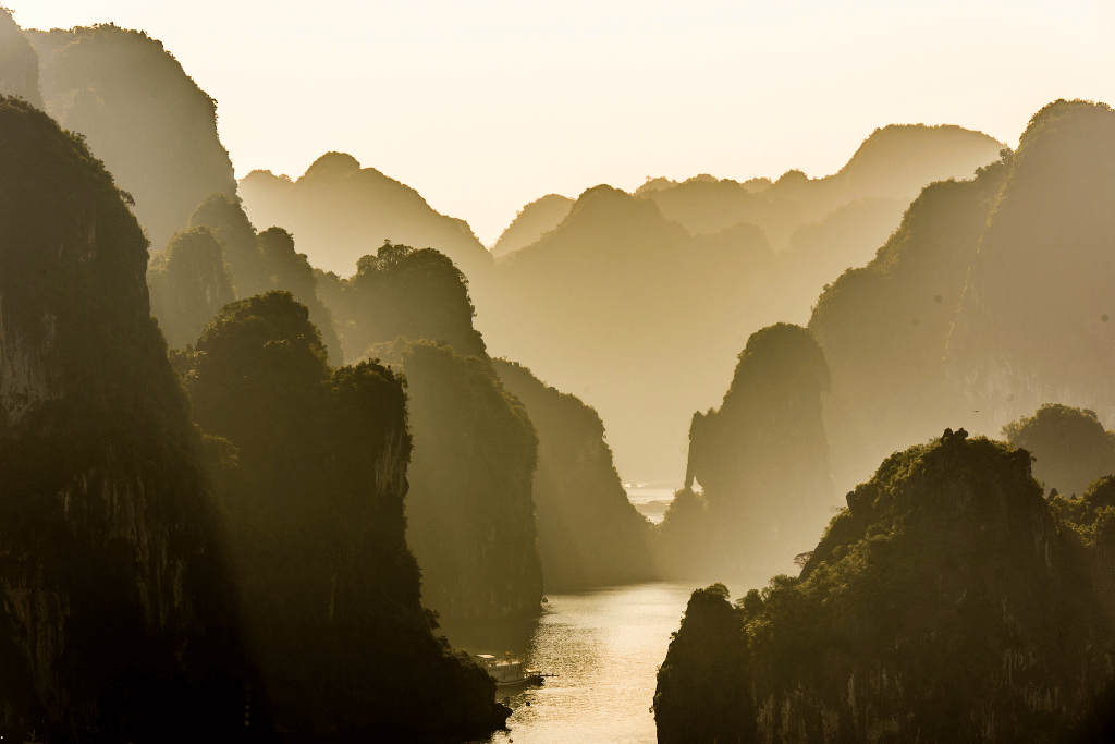 Layers of limestone peaks fading into haze above a narrow channel in Ha Long Bay