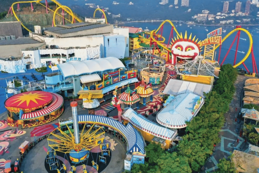 Aerial view over Ocean Park's hilltop rides and carnival midway with the sea and city behind