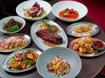 An overhead spread of plated dishes including salads, ribs and croquettes on a table
