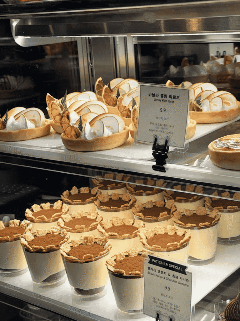 Vanilla flan tarts and tiramisu cups in a lit bakery display case with Korean price labels