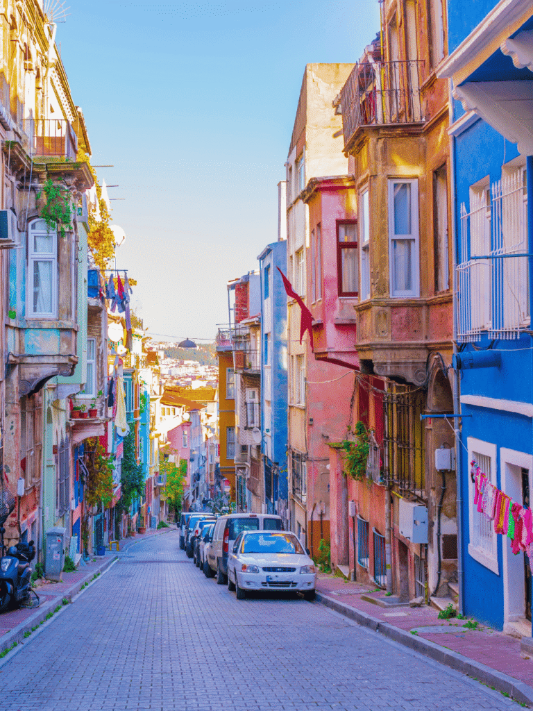 A steep, narrow Istanbul street lined with pastel-painted houses and parked cars