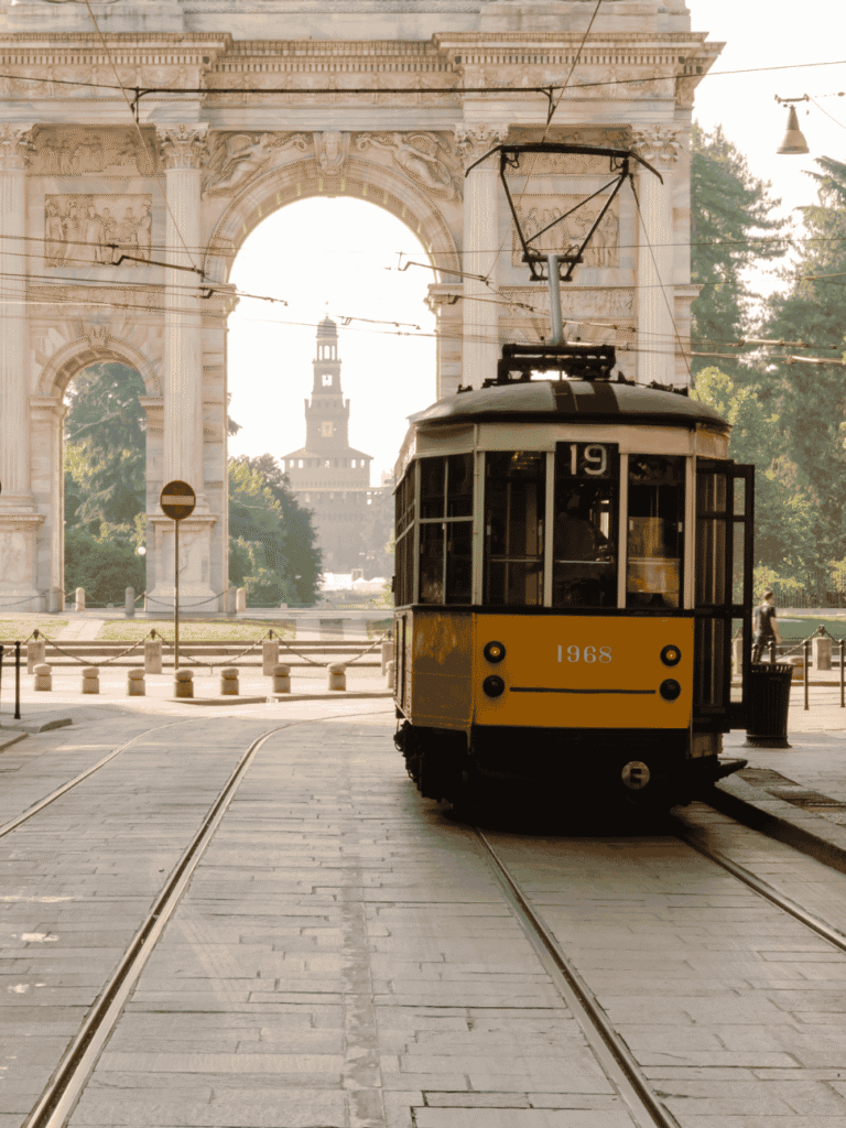 A vintage yellow Milan tram passing the Arco della Pace, with Castello Sforzesco framed in the arch