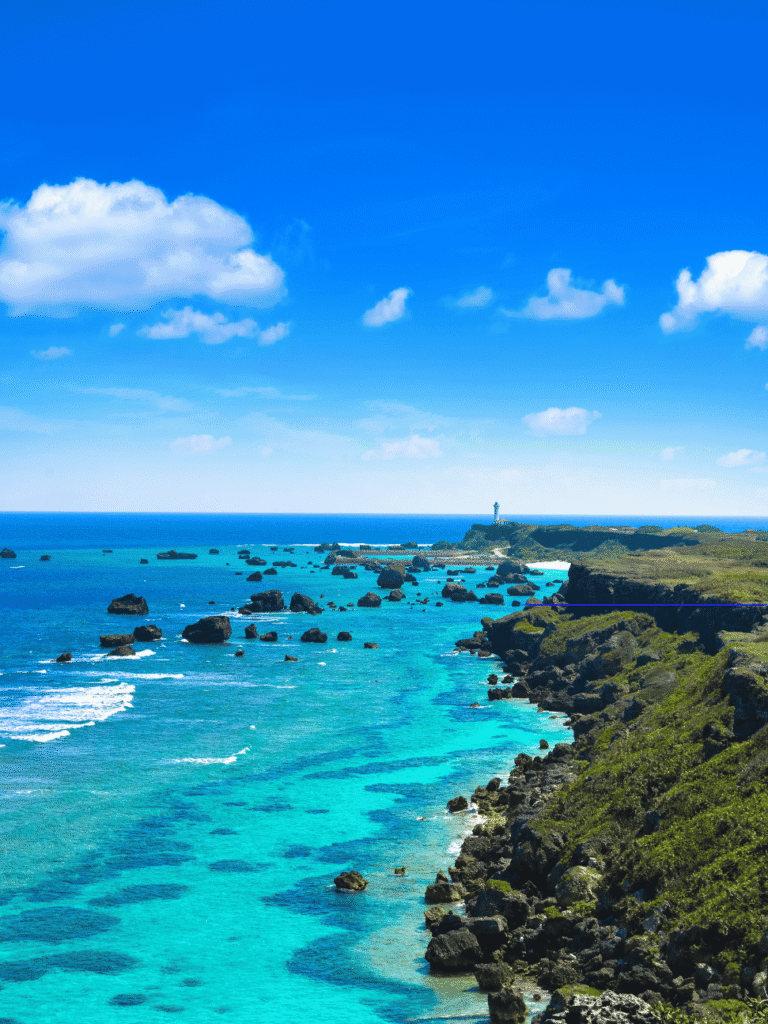 Turquoise reef water and rocky outcrops along a green cape, with a lighthouse in the distance