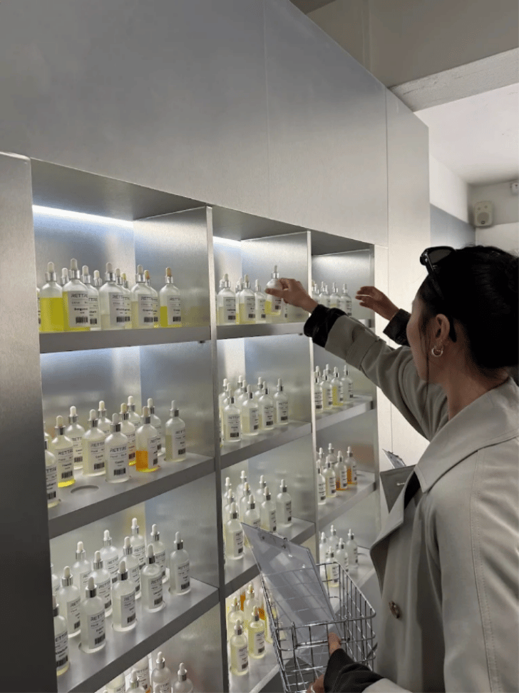 A customer reaching for a labelled RETTRE fragrance bottle on lit metal shelving