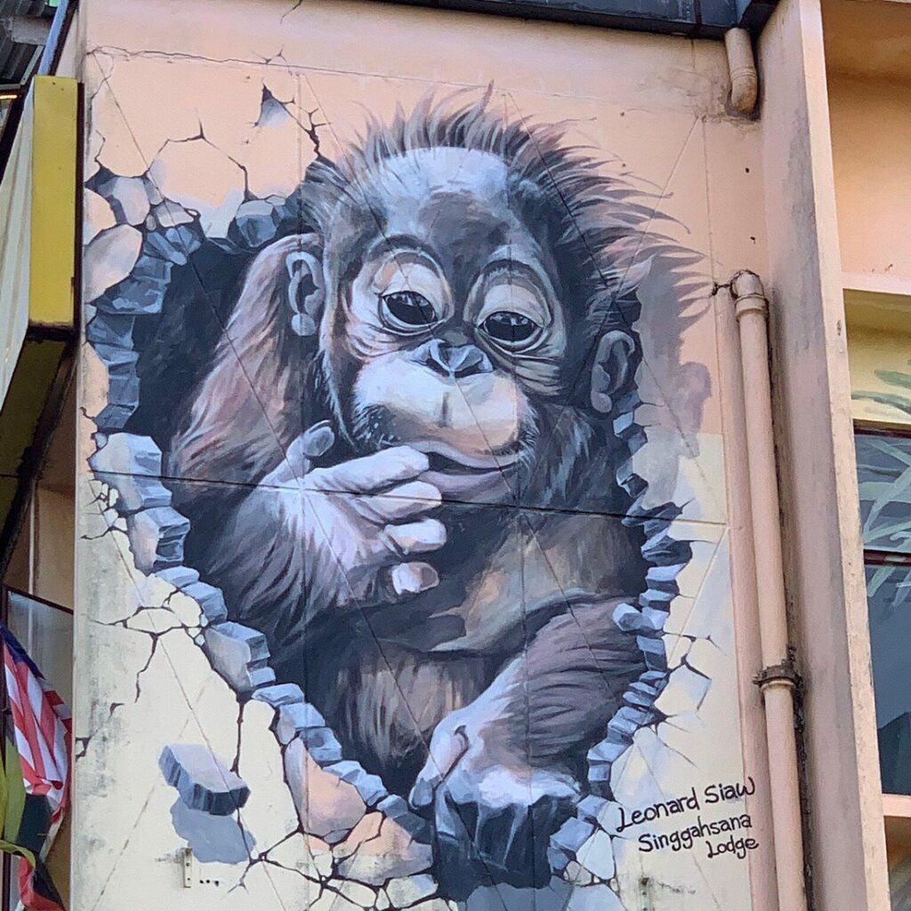 Mural of a baby orangutan appearing to push through a cracked wall, signed Leonard Siaw