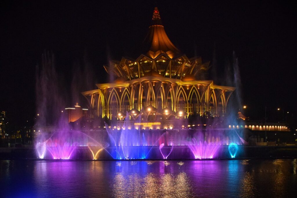 Coloured fountain jets rising in front of the floodlit State Assembly building at night