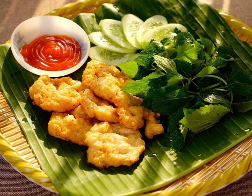Golden fried squid cakes on a banana leaf with chilli dipping sauce, cucumber and herbs